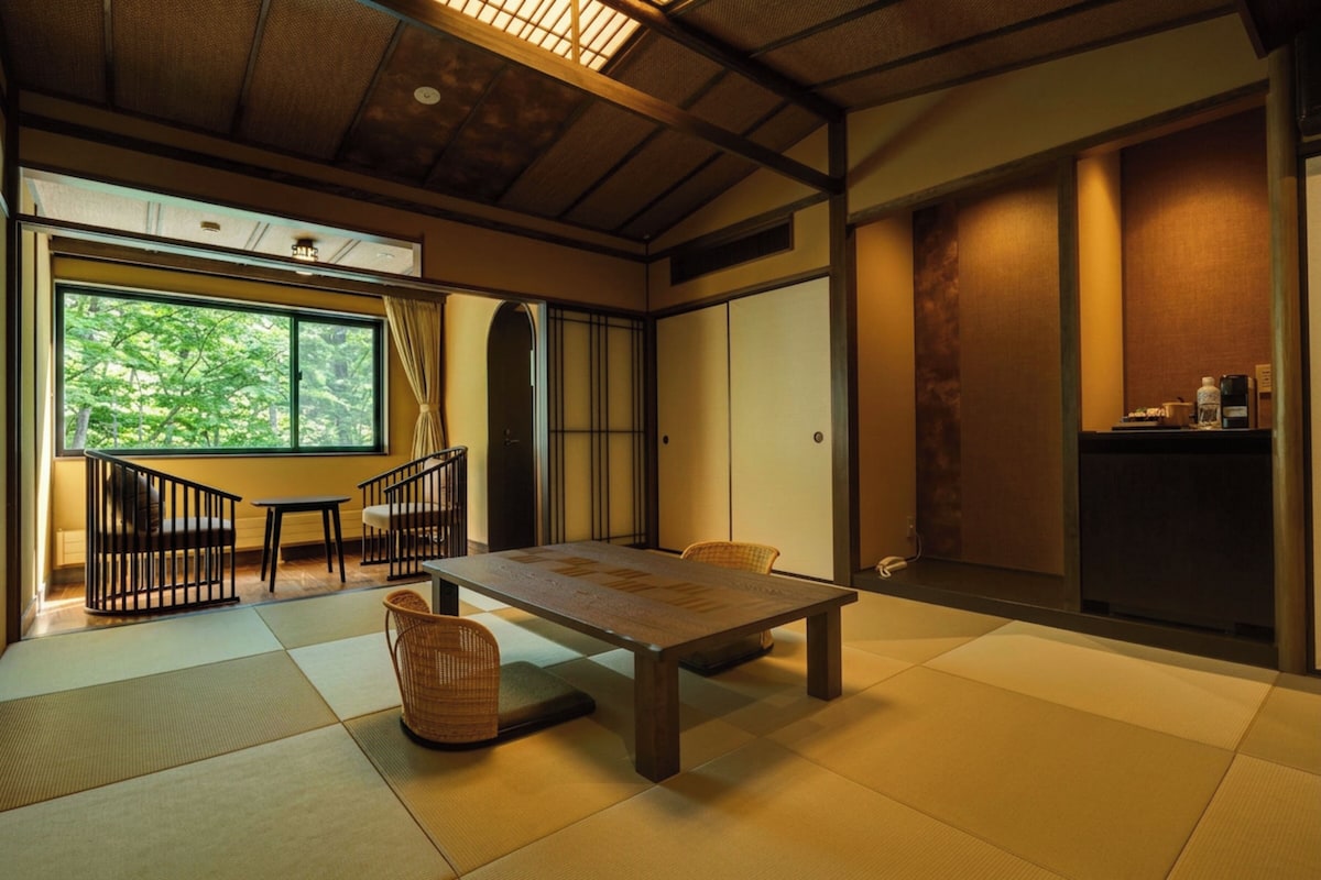 A traditional Japanese room with tatami flooring, a low table, and a view of greenery outside.