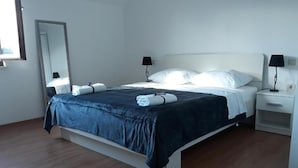 A neatly made bed with a dark blue bedspread and white pillows, a bedside table with a lamp, and a large mirror on the wall.