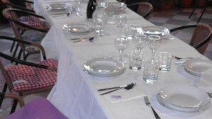 A dining table set with plates, glasses, and cutlery, surrounded by chairs.