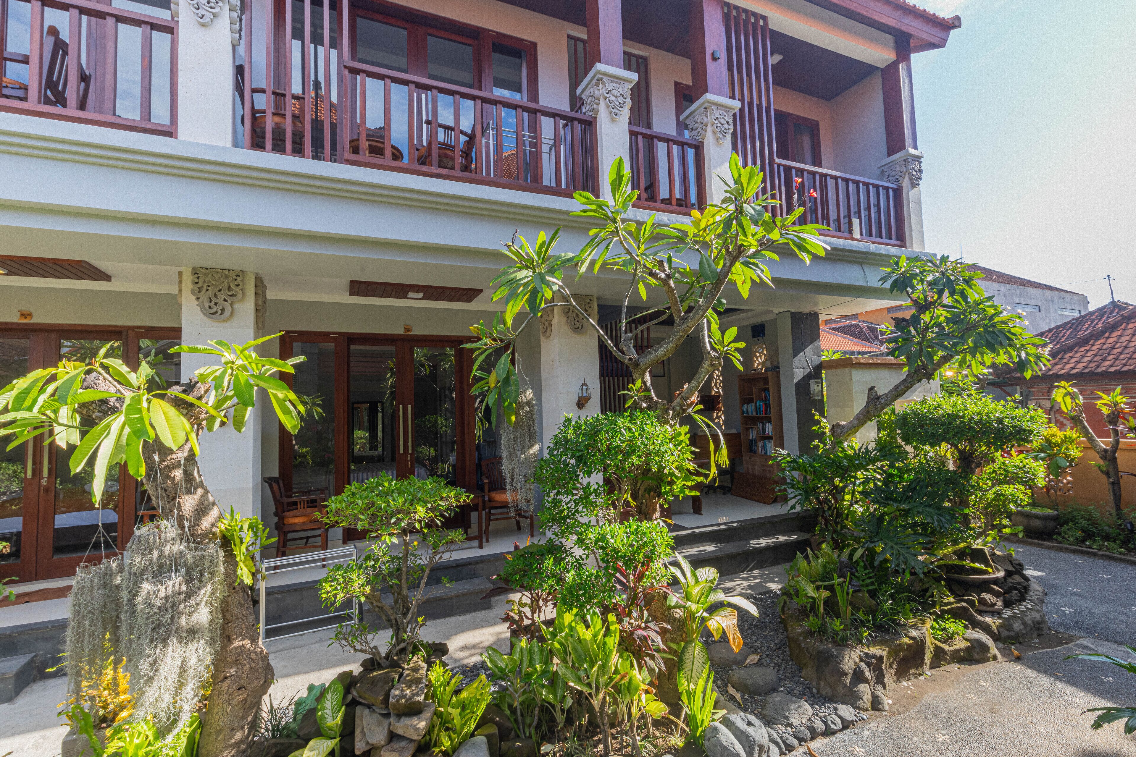 A two-story building with a balcony, surrounded by various plants and trees.