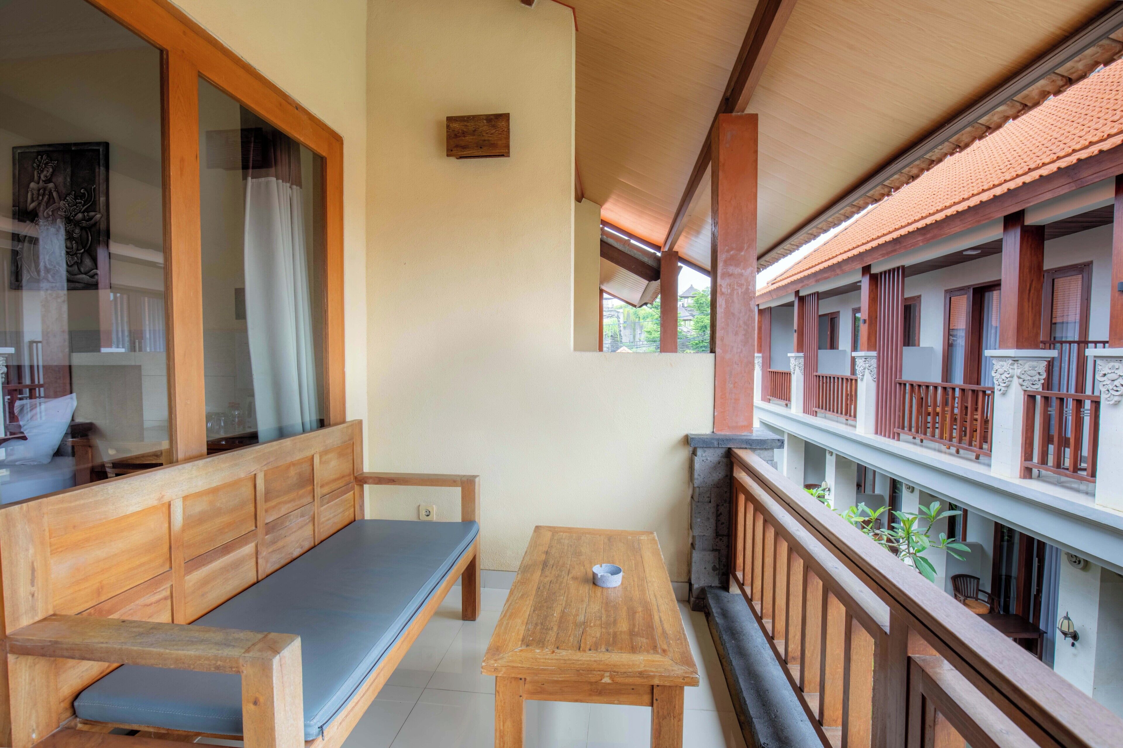 A traditional wooden balcony with a bench and a table, a tiled floor, and a view of a building with a tiled roof.