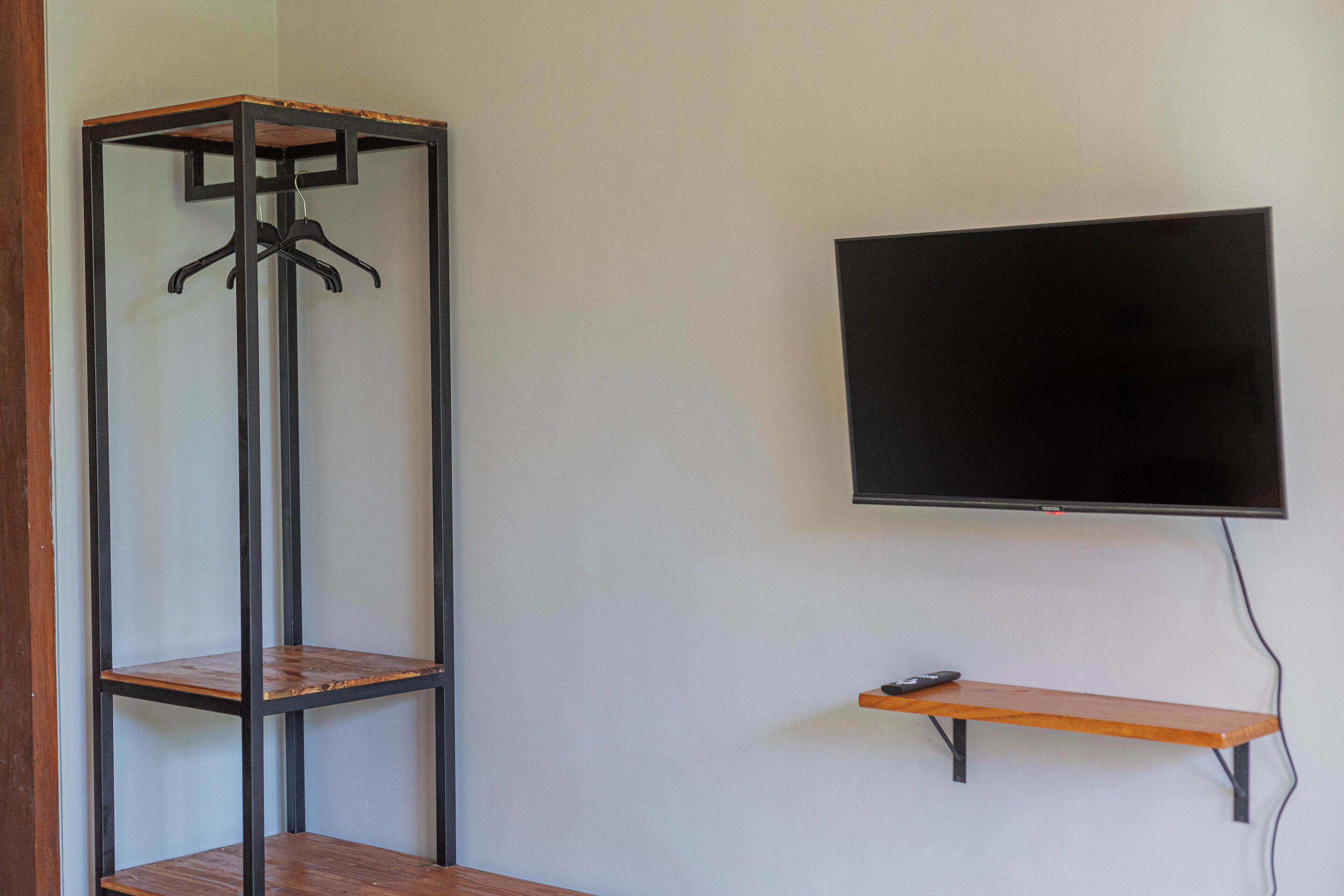A room with a TV mounted on the wall, a wooden shelf, and a metal shelving unit with a coat rack.