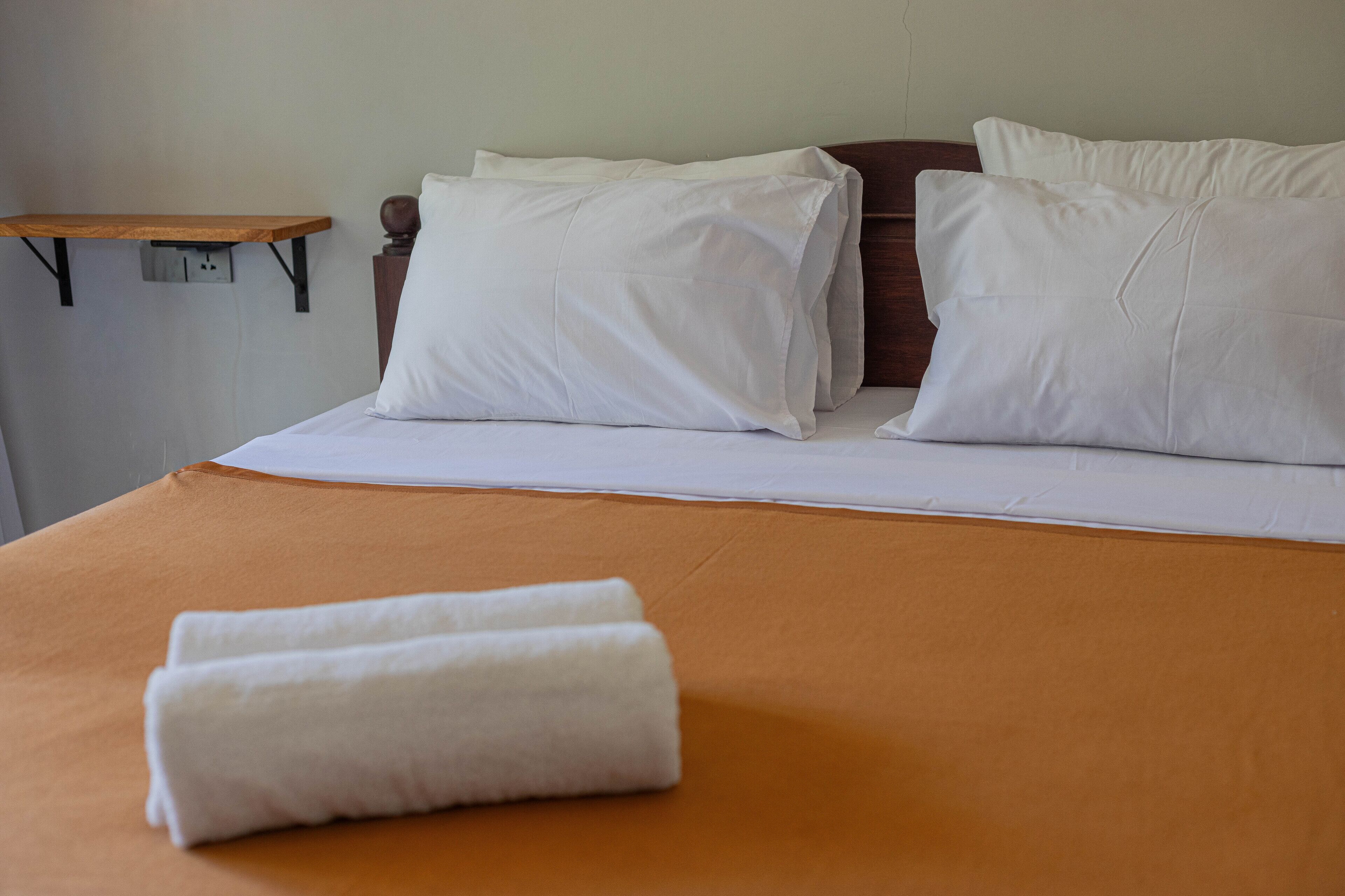 A neatly made bed with white linens and a folded towel on an orange bedspread.