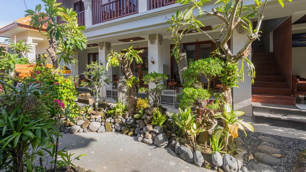 A two-story building with a balcony, surrounded by tropical plants and a stone pathway. - Donahome (Denpasar)