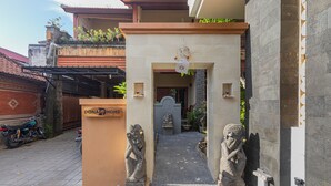 A traditional Balinese entrance with a stone gate, a small shrine, and a motorcycle parked outside. - Donahome (Denpasar)