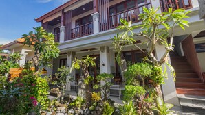 A two-story house with a balcony, surrounded by various plants and trees. - Donahome (Denpasar)