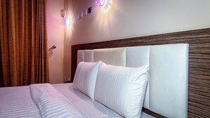 A hotel room with a bed, white bedding, a wooden headboard, and wall-mounted lights. - Mo-House Hotel and Event Center (Abuja)