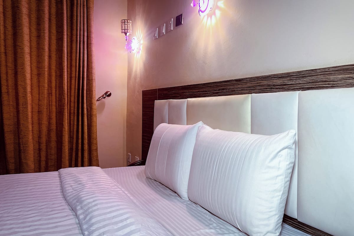 A hotel room with a bed, white bedding, a wooden headboard, and wall-mounted lights.