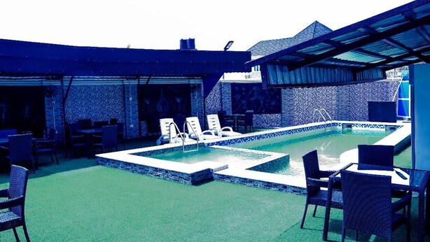 An outdoor pool area with lounge chairs and tables, surrounded by a covered patio. - Mo-House Hotel and Event Center (Abuja)