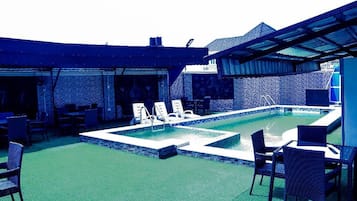 Un espace piscine extérieur doté de chaises longues et de tables, entouré d’une terrasse couverte.