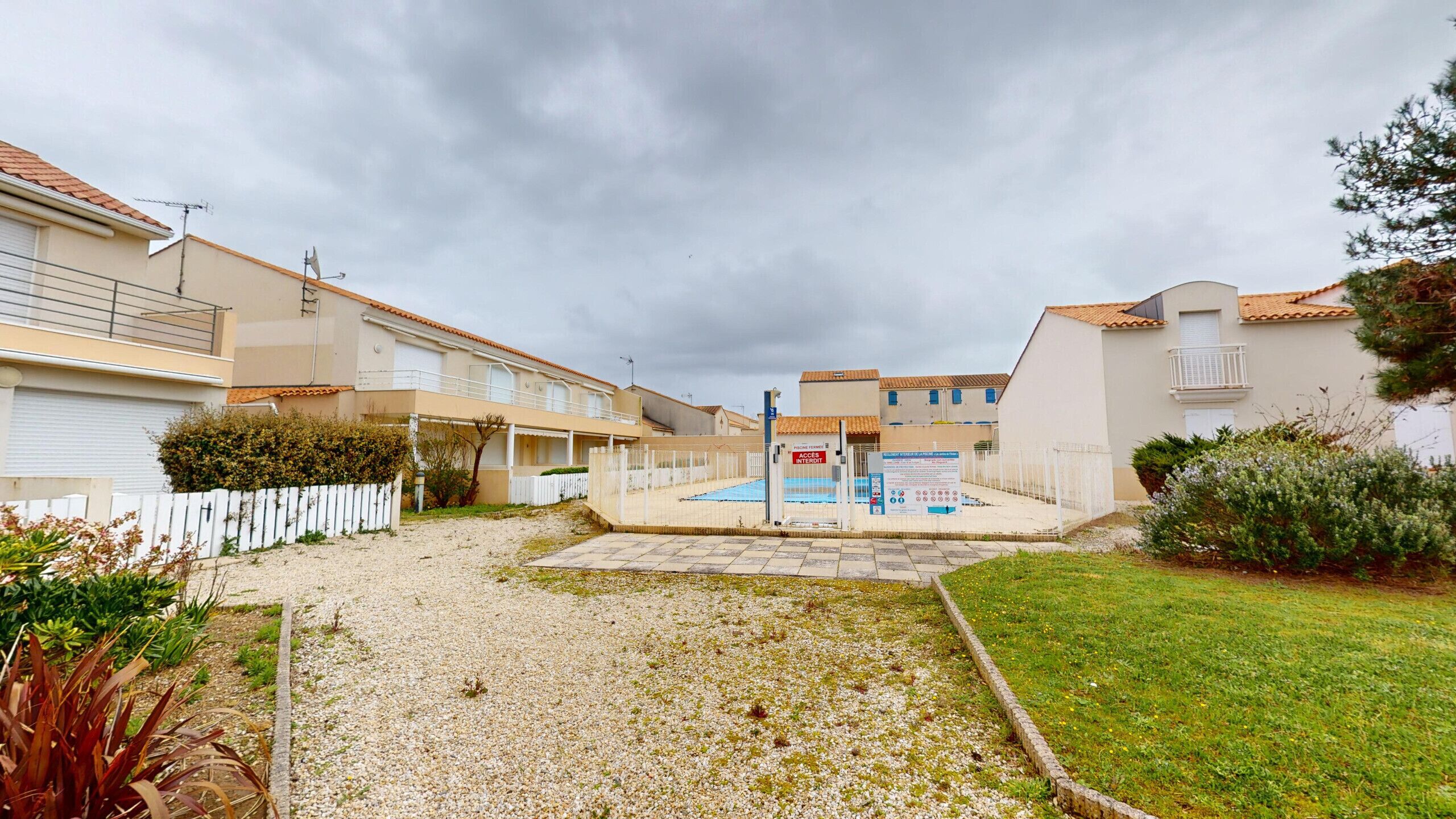 Un quartier résidentiel doté d’une piscine, de clôtures blanches et de maisons aux toits en tuiles.