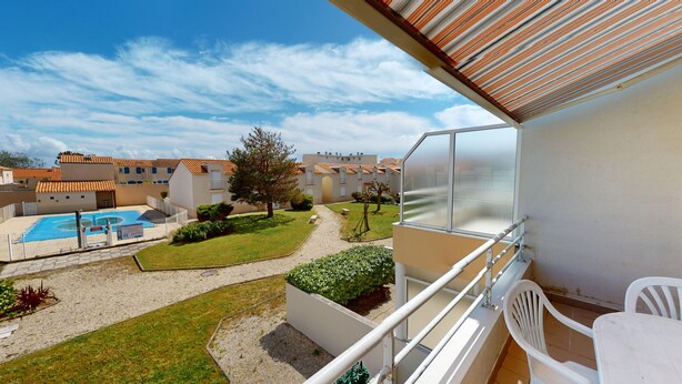 Un balcón con vistas a una piscina, un jardín y edificios colindantes.