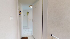 Un pasillo estrecho con paredes blancas, suelo de baldosas y una puerta con la etiqueta 