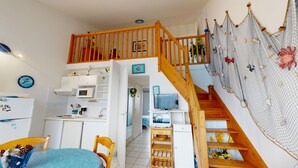 Cocina compacta con microondas, estufa y pileta. Una escalera de madera con barandilla de red conduce a un segundo piso.