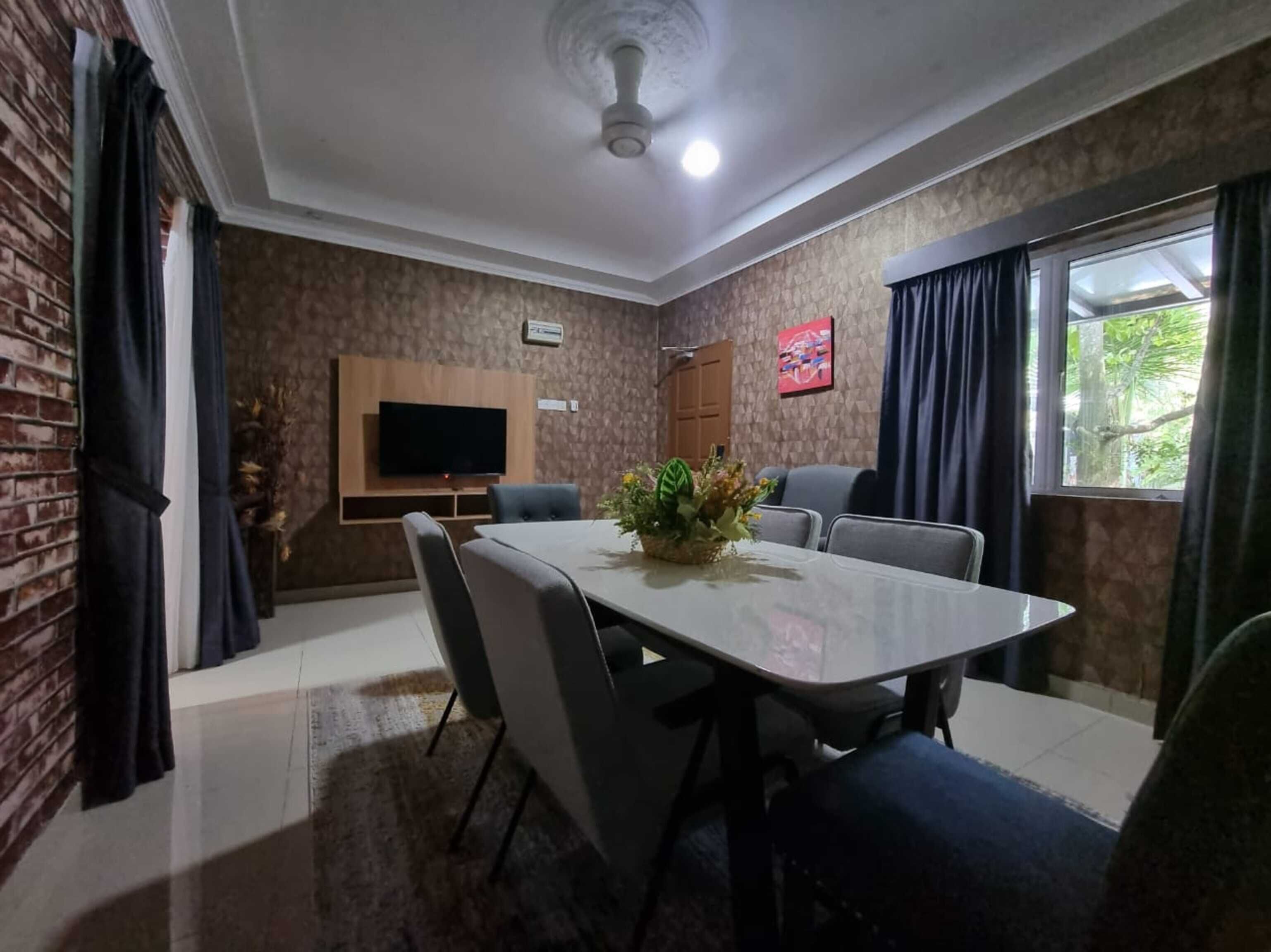 A dining area with a table, chairs, a television mounted on the wall, and a window with curtains.