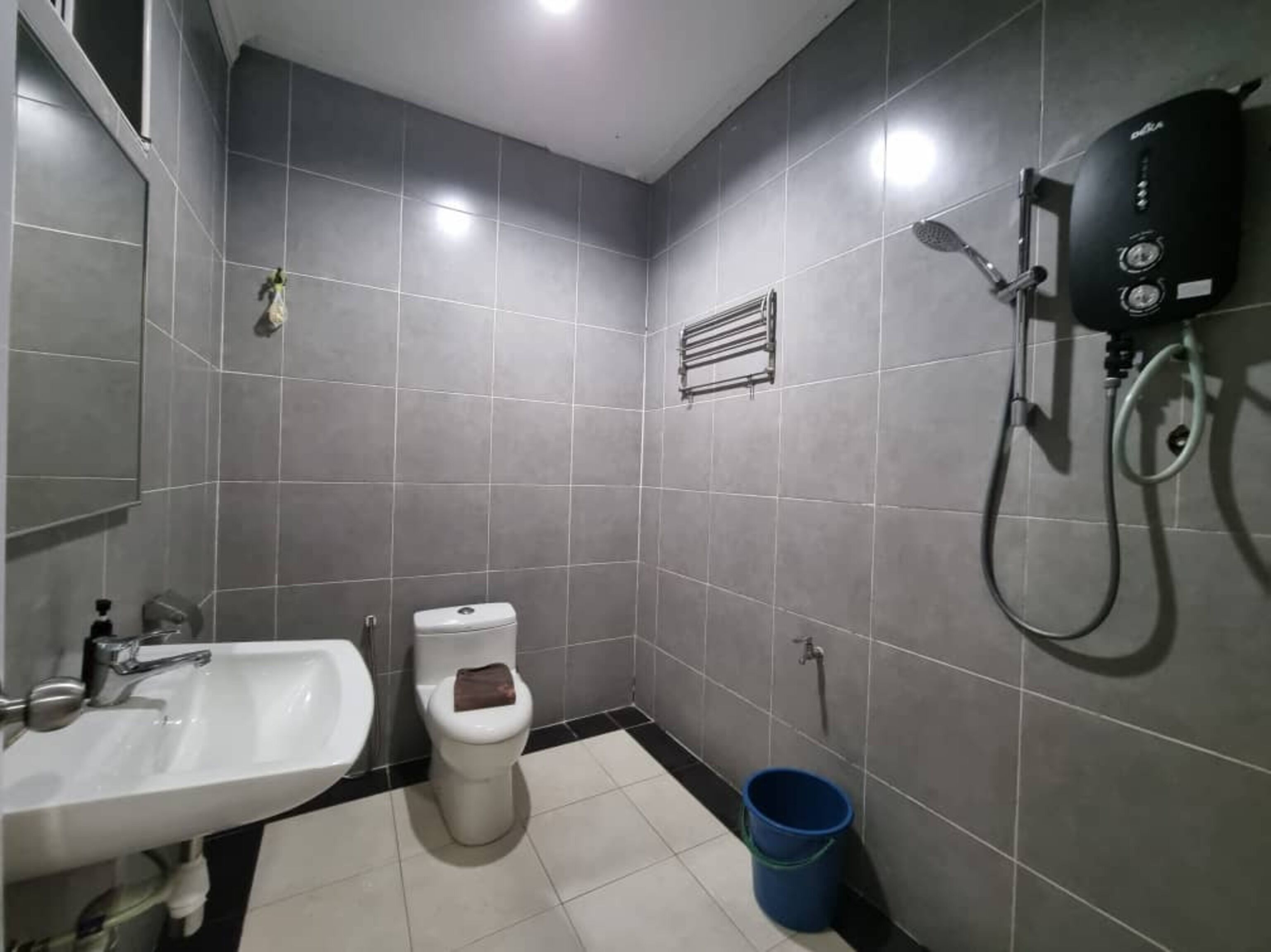 A bathroom with a white sink, a toilet, a shower, and a blue bucket.