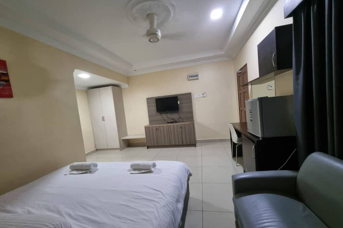 Habitación de hotel con cama, sofá, televisor, minibar y ventilador de techo.