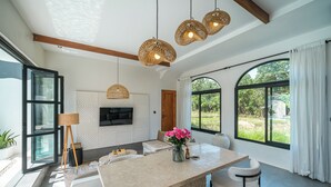 A modern kitchen with a central island, pendant lights, and a large window with curtains. - Villa Honey (Canggu)