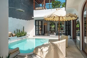 A poolside area with a lounge chair, a sun umbrella, and a view of the pool.