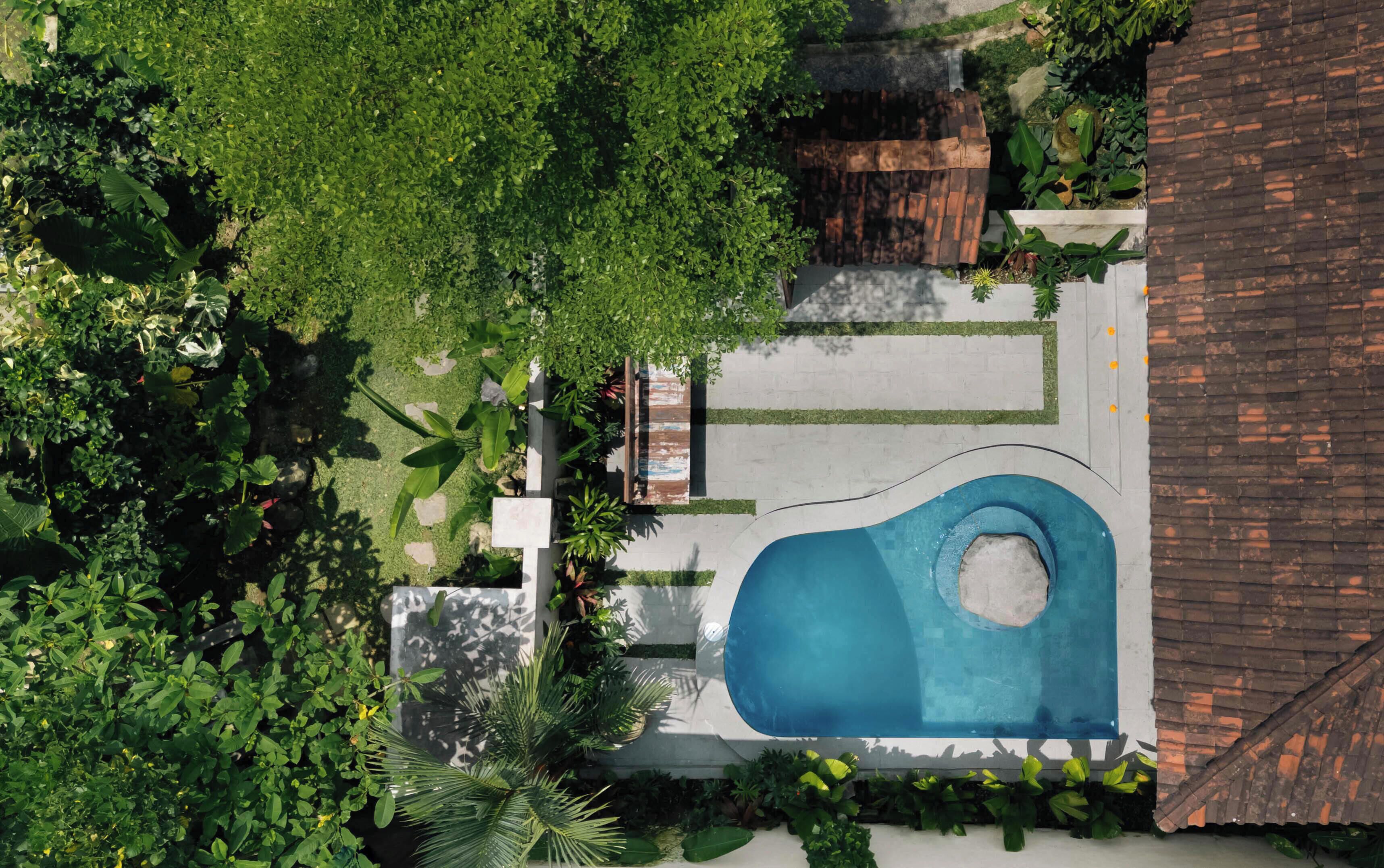 An aerial view of a property with a swimming pool, surrounded by greenery and a brick structure.