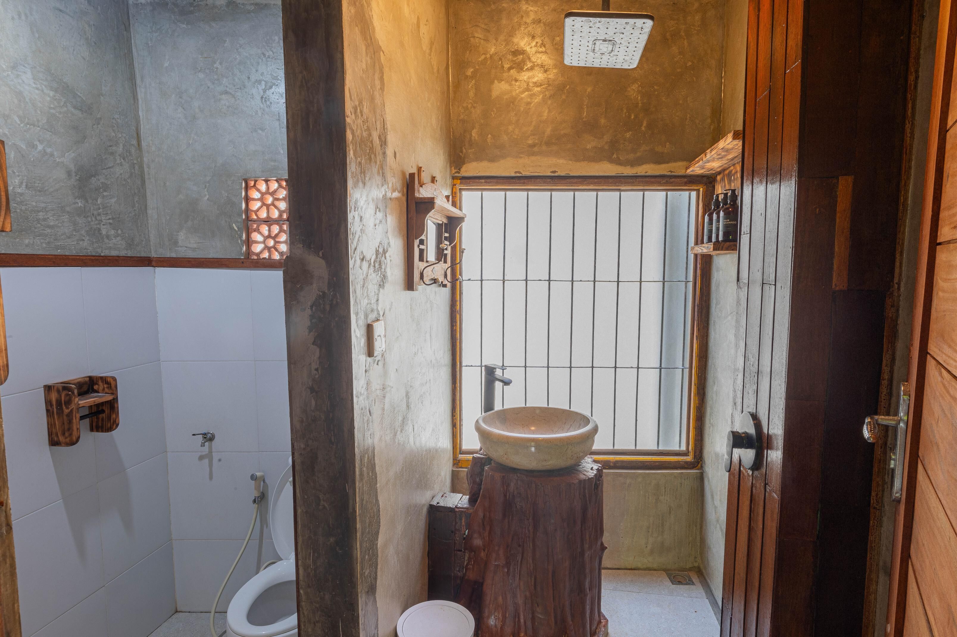 Un baño pequeño y funcional con un taburete de madera, un inodoro blanco y un estante de madera.