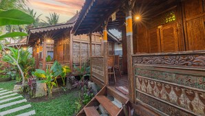 A traditional wooden building with a covered porch, steps leading to the entrance, and a garden with tropical plants.