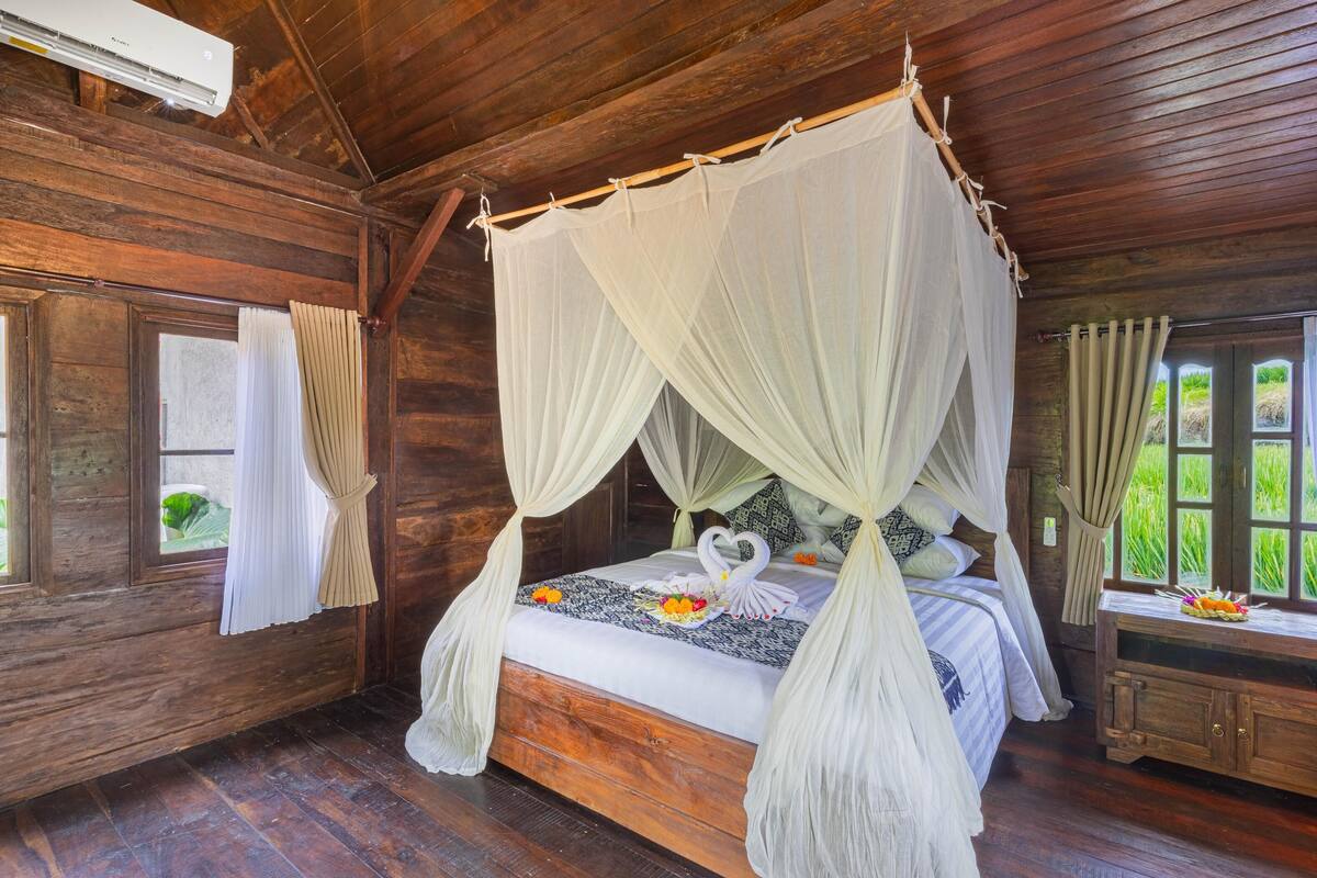 A wooden room with a four-poster bed, a wooden cabinet, and a window with curtains.