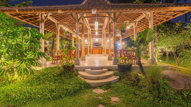 A gazebo-style structure with a tiled roof, surrounded by lush greenery and stone steps leading to the entrance.