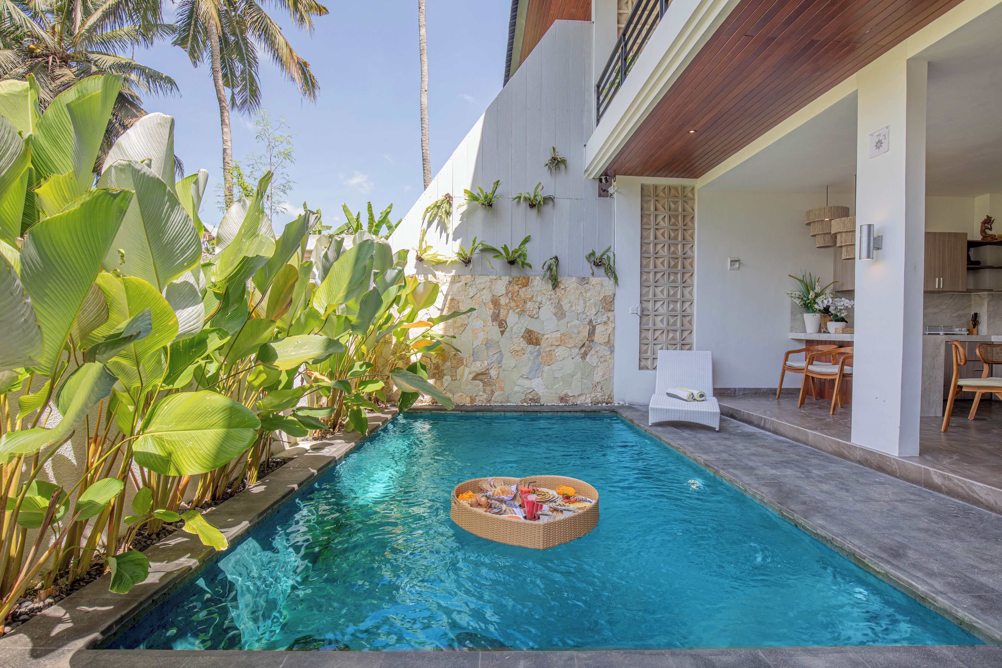 Una piscina con un bar flotante, rodeada de plantas tropicales y un muro de piedra.