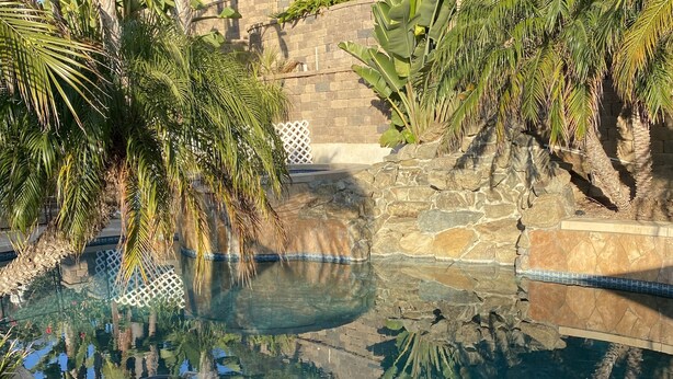 Una piscina cristal·lina envoltada de plantes tropicals i parets de pedra.