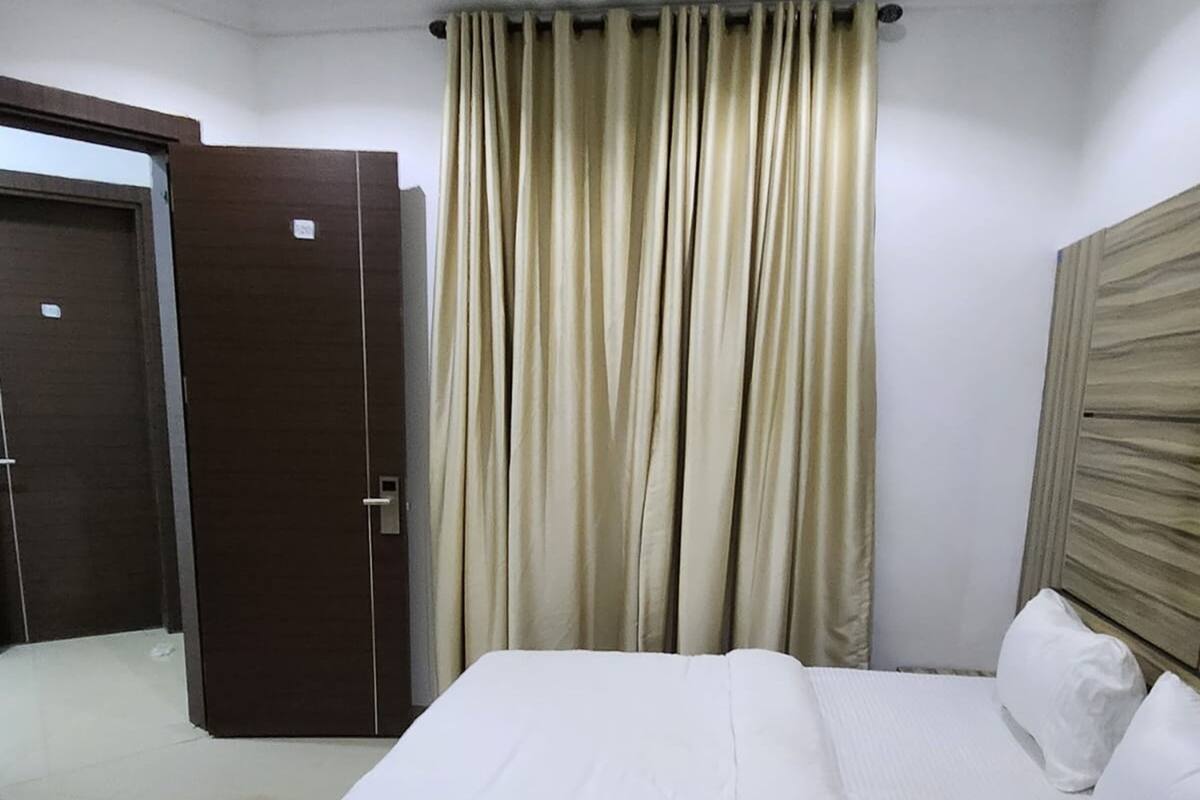A hotel room with a bed, curtains, a wooden headboard, and a door.