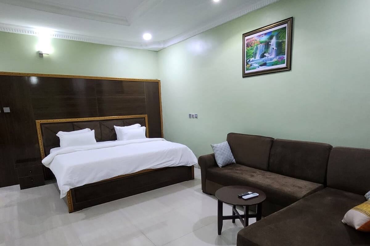 A hotel room with a large bed, a sofa, a small table, and a framed picture on the wall.