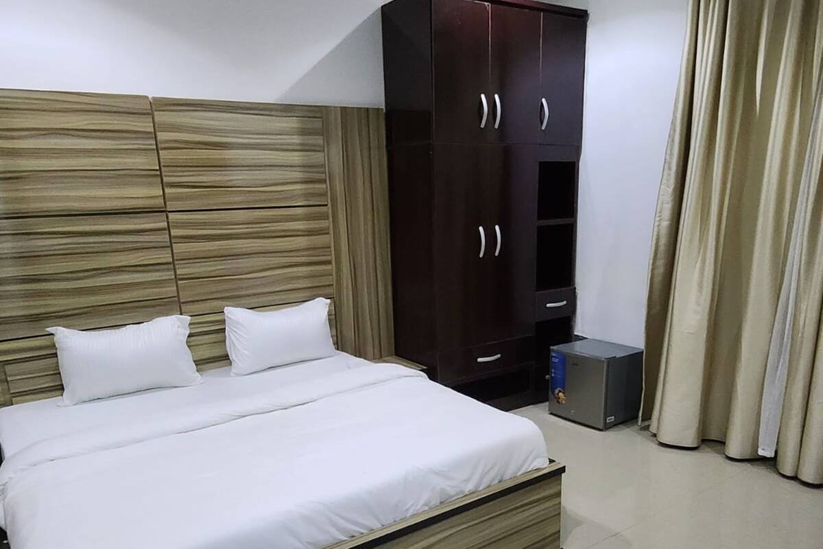 A bedroom with a large bed, wooden headboard, dark wardrobe, and beige curtains.