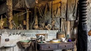 A rustic kitchen with wooden furniture, a stone wall, and various kitchen utensils hanging on the wall.