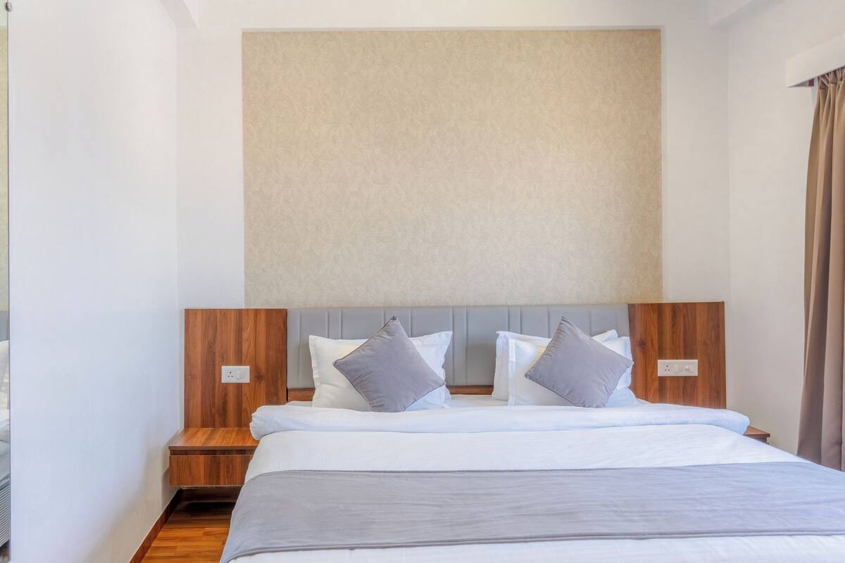 Una cama bien hecha con cabecera de madera, dos mesitas de noche y una pared de color neutro.