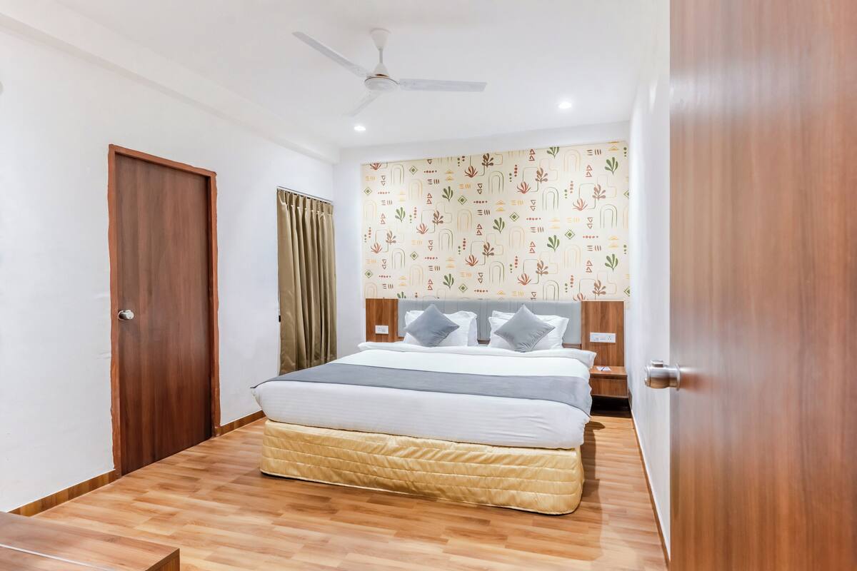 Un dormitorio con suelo de madera, una cama con colchón acolchado, un ventilador de techo y un papel tapiz estampado.