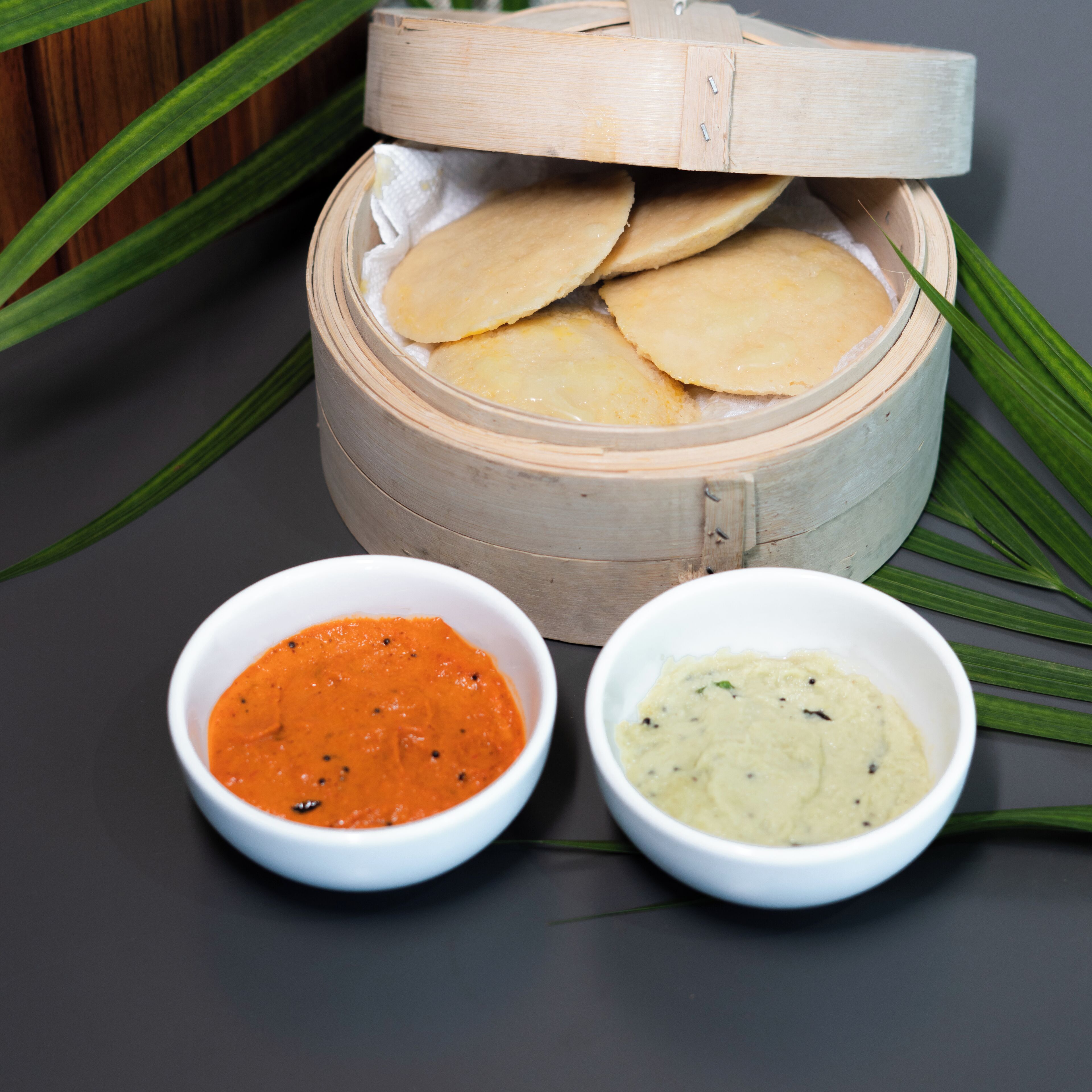 A bamboo steamer with several flatbreads and two bowls of sauces.