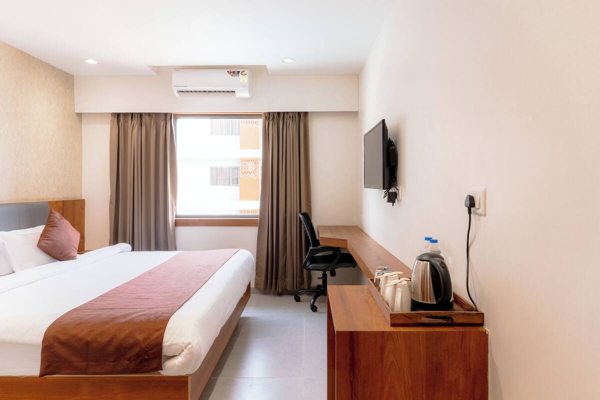 Habitación de hotel con cama, escritorio, silla, televisor y cafetera.
