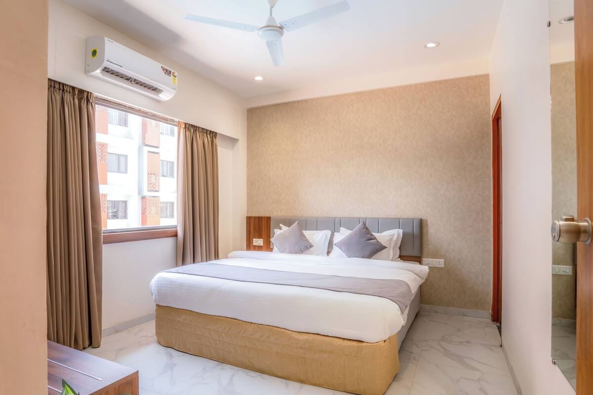 Habitación de hotel con cama, aire acondicionado, ventilador de techo y ventana con cortinas.