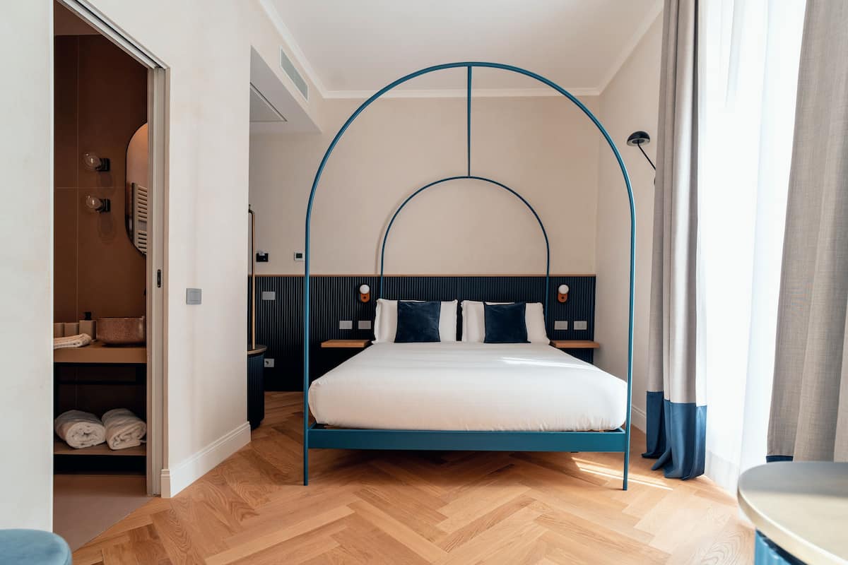 A modern bedroom with a bed under a blue arch, wooden flooring, and a visible closet with towels.