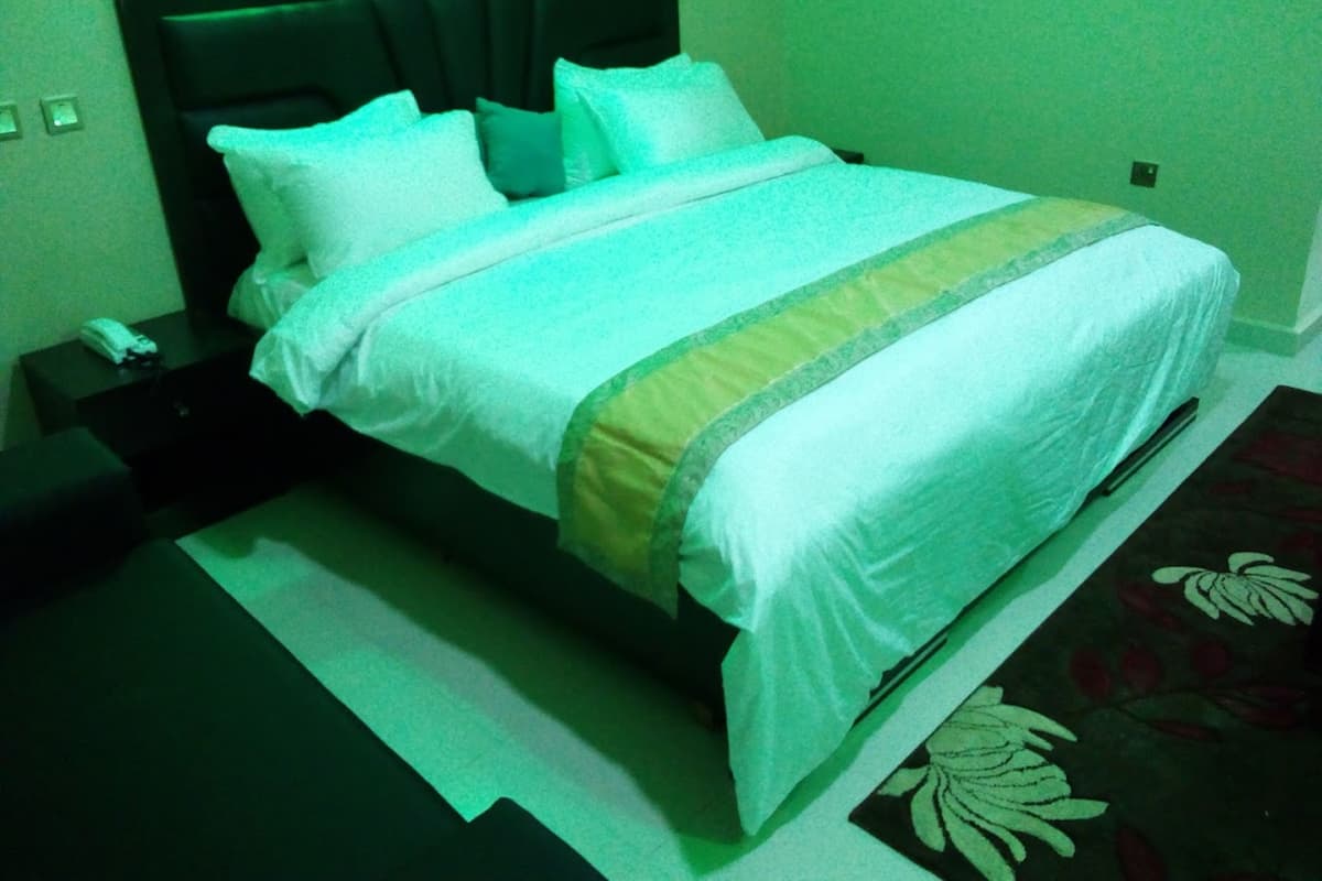 A neatly made bed with white linens and a green accent, a bedside table with a phone, and a patterned carpet.