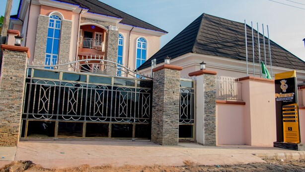A two-story house with a gated entrance, a balcony, and a flag on the right side. - Prismar International Hotel (Uyo)