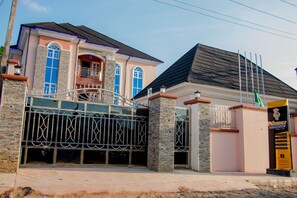 A two-story house with a gated entrance, a balcony, and a flag on the right side. - Prismar International Hotel (Uyo)