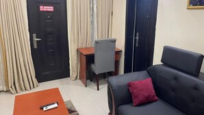 A living room with a sofa, a coffee table, a desk with a chair, and a door with a 'No Smoking' sign. - Prismar International Hotel (Uyo)