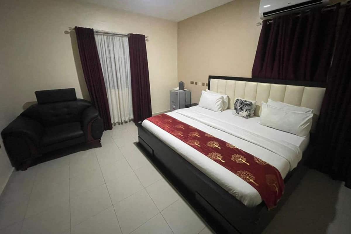 A bedroom with a bed, a chair, an air conditioner, and curtains.