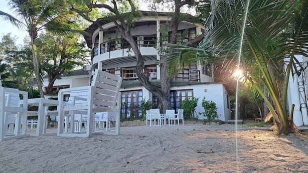 A beachfront property with a multi-level building, outdoor seating area, and palm trees. - Silver sand beach hotel (Malindi)