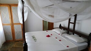 A bed with a canopy, white linens, and a name embroidered on the bedspread. - Silver sand beach hotel (Malindi)