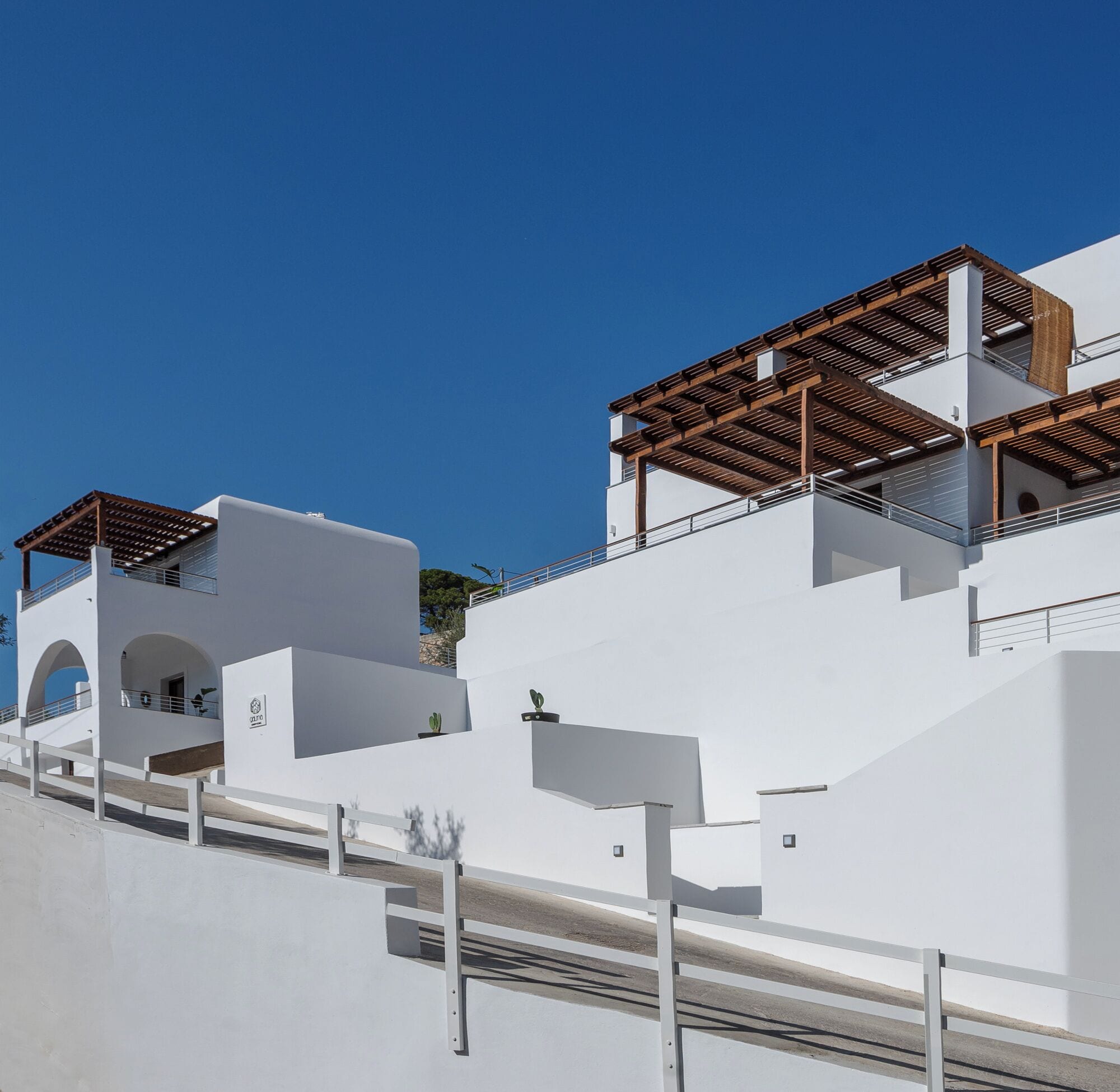 Un edificio moderno blanco con techo plano y una pérgola de madera en el nivel superior, con fachada blanca.