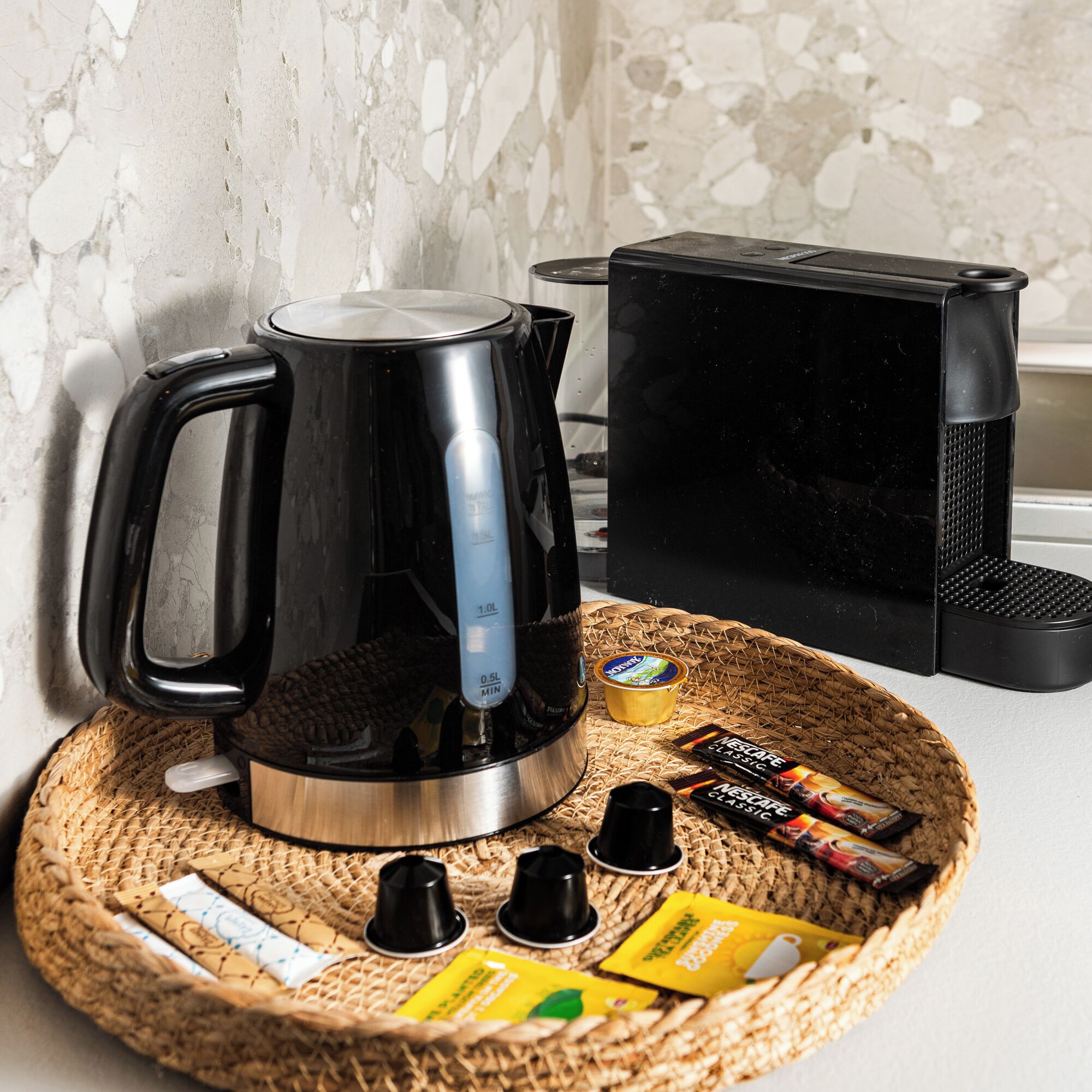 A coffee maker on a woven tray with coffee pods and a kettle.