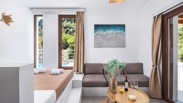 Una habitación moderna con una cama, un sofá, una mesita con una botella y vasos, y un cuadro en la pared.